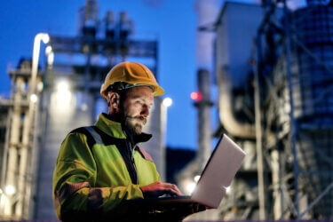 Male engineer using laptop during night shift outside factory.