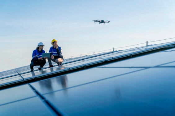 Two engineers stand between solar panels and look at drone.