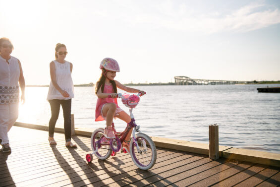Two family members walk behind a young girl learning how to bike along Lake Charles.